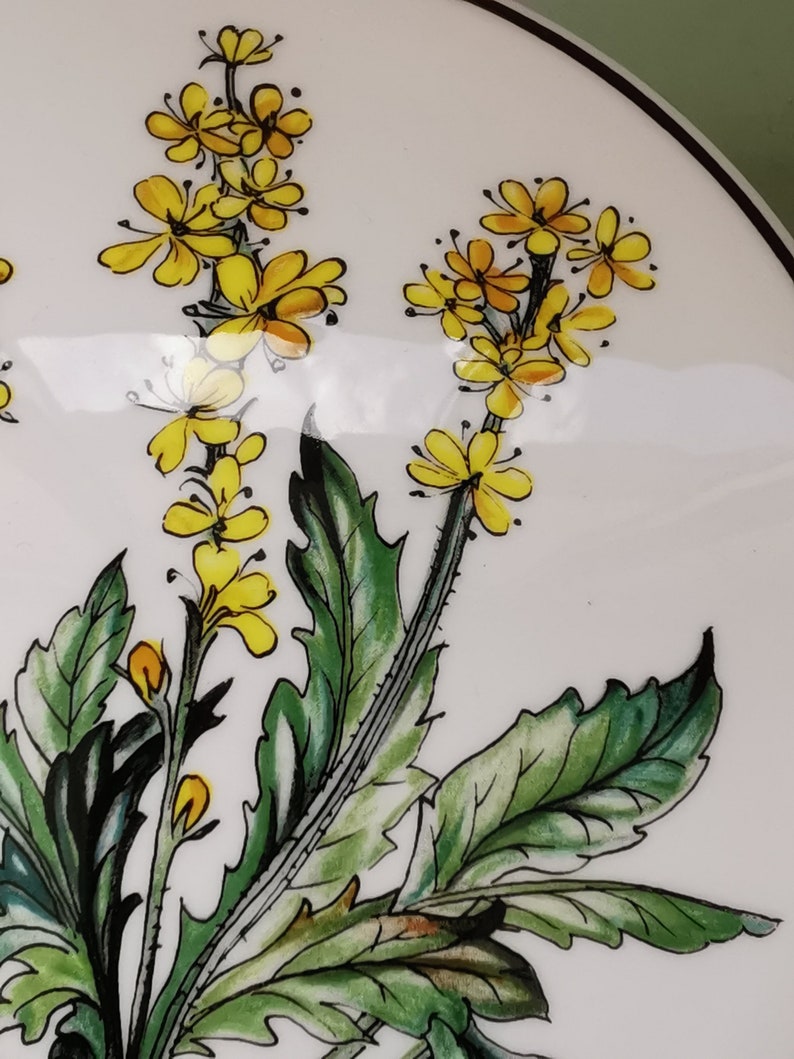 May include: A white ceramic plate with a hand-painted design of yellow flowers and green leaves.
