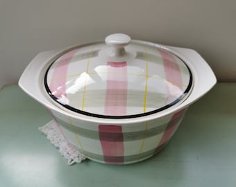 May include: A white ceramic casserole dish with a pink and gray plaid pattern and a clear glass lid.