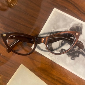 May include: Brown cat-eye glasses with gold accents on the temples.