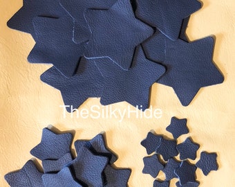 May include: A collection of navy blue leather star shapes in various sizes. The stars are arranged in three groups on a beige surface. The text "TheSilkyHide" is visible in the center of the image.