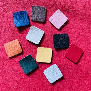 May include: Ten different colored leather squares, each with a unique texture. The squares are arranged in a circle on a red background.