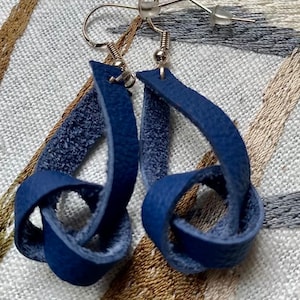 May include: A pair of blue leather earrings with a knotted design. The earrings are made from soft, supple leather and have a simple, elegant look.