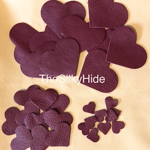 May include: A collection of burgundy leather heart shapes in various sizes. The hearts are arranged in two groups, with the larger hearts in the top left and the smaller hearts in the bottom right. The text "The Silky Hide" is visible in the centre of the image.