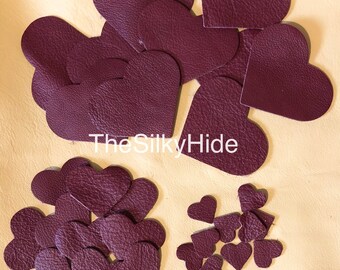May include: A collection of burgundy leather heart shapes in various sizes. The hearts are arranged in two groups, with the larger hearts in the top left and the smaller hearts in the bottom right. The text "The Silky Hide" is visible in the center of the image.