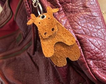 May include: A burgundy leather bag with a brown leather animal keychain attached to the zipper pull.