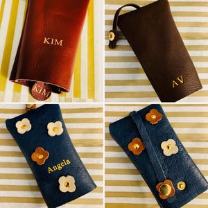 May include: Four leather keychains in various colors: burgundy, brown, and navy blue. The burgundy keychain has "KIM" embossed on it. The brown keychain has "AV" embossed. The navy blue keychains have flower accents and the name "Angela" embossed.