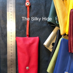 May include: A red leather key holder with a snap closure and a matching strap. The key holder is shown next to a ruler. The text "The Silky Hide" is visible. Other colorful leather key holders are in the background.