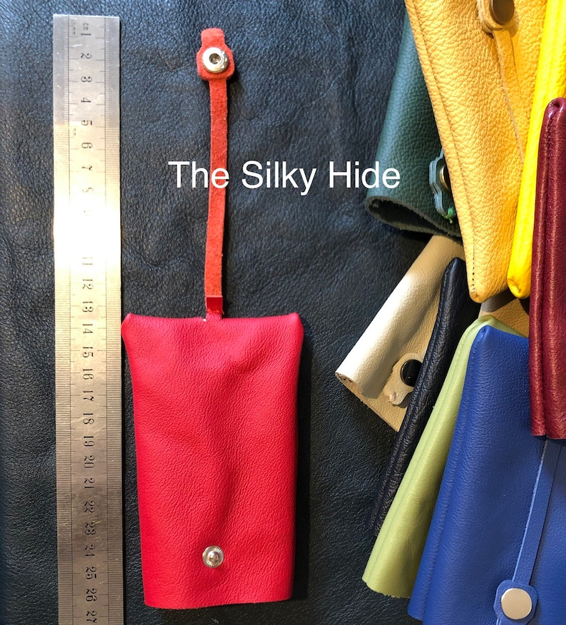 May include: A red leather key holder with a snap closure and a matching strap. The key holder is shown next to a ruler. The text "The Silky Hide" is visible. Other colorful leather key holders are in the background.