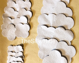 May include: A stack of 15 white leather cloud-shaped patches. The patches are arranged in a pile, with the largest patch at the bottom and the smallest patch at the top. The patches are all the same shape, but they vary in size. The patches are made of a soft, supple leather.