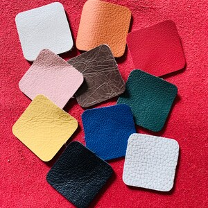 May include: Assortment of ten square leather swatches in various colors, including white, orange, red, pink, brown, green, yellow, blue, black, and gray. The swatches are arranged on a red surface.