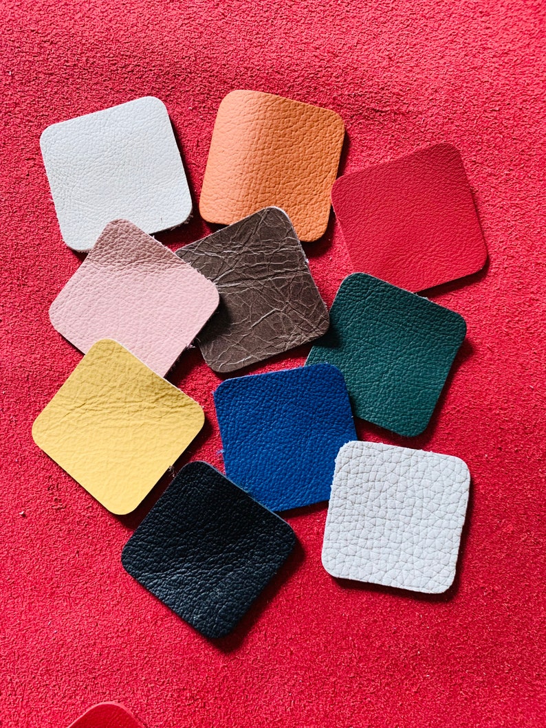 May include: Assortment of ten square leather swatches in various colors, including white, orange, red, pink, brown, green, yellow, blue, black, and gray. The swatches are arranged on a red surface.