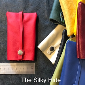 May include: A red leather pouch with a snap closure and a strap. Other colorful leather pouches in green, yellow, cream, black, blue, and burgundy are also visible. The text "The Silky Hide" is at the bottom.