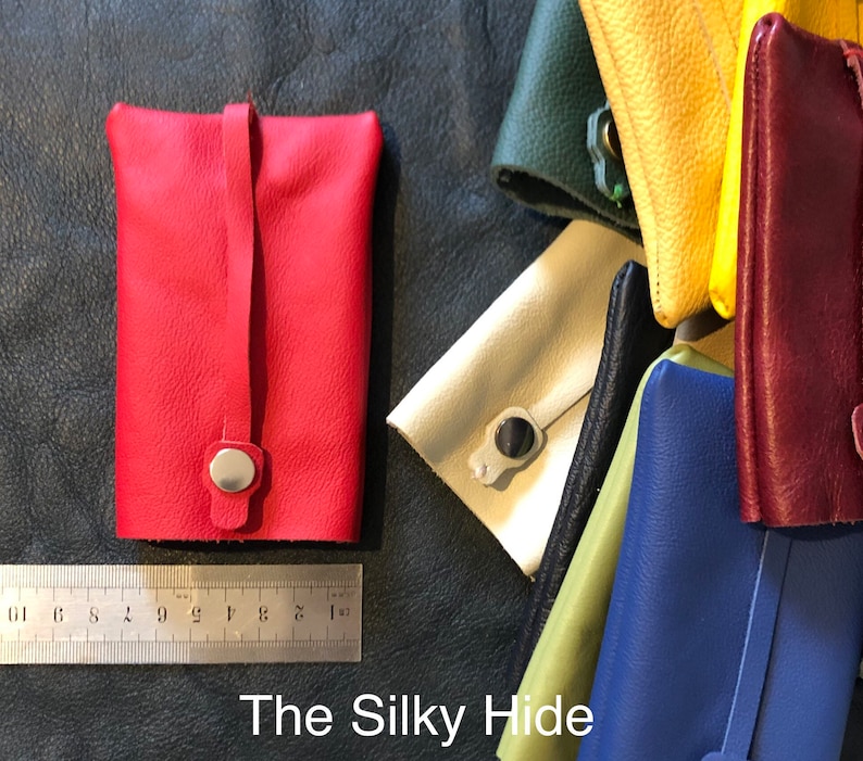 May include: A red leather pouch with a snap closure and a strap. Other colorful leather pouches in green, yellow, cream, black, blue, and burgundy are also visible. The text "The Silky Hide" is at the bottom.