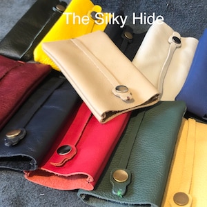 May include: A collection of colorful leather key holders in various shades, including red, yellow, green, and blue. Each holder features a snap closure and a strap detail. The text "The Silky Hide" is visible in the image.