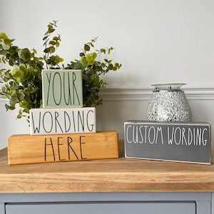 May include: Wooden blocks with custom text in various colours. The blocks are painted in green, white, grey, and natural wood tones. The text on the blocks reads "YOUR", "WORDING HERE", and "CUSTOM WORDING" in a handwritten style.