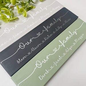 May include: Four rectangular wooden signs in shades of gray, black, and green. Each sign has the words "Our family" in white script, with names and hearts below. Decorative home decor.