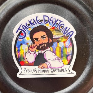 Puede incluir: Una pegatina blanca con una ilustración de dibujos animados de un hombre con barba y bigote. Lleva una camisa rosa y un chaleco negro. El texto "Jackie Daytona Regular Human Bartender" está escrito en la pegatina.