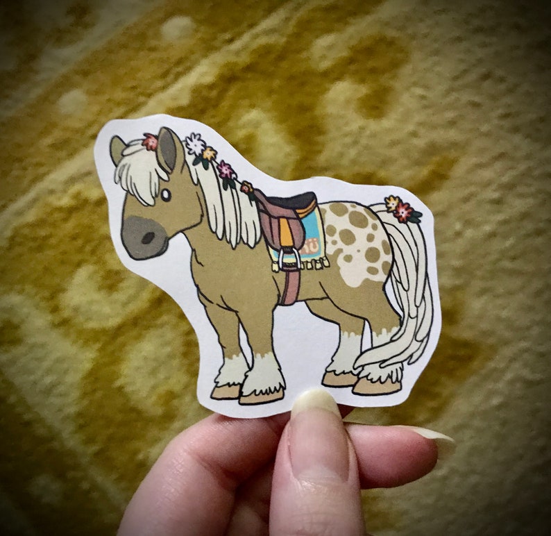 May include: A brown and white spotted horse with a brown saddle and a floral crown. The horse is standing on a white background.