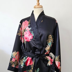 May include: Black satin robe with a floral print featuring pink, red, and gold accents. The robe has a tie belt and two pockets.