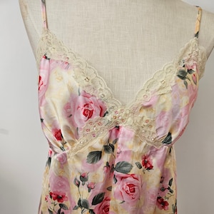 May include: A pale yellow satin slip dress with a floral print of pink roses and green leaves. The dress has a lace trim around the neckline and straps.