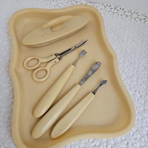May include: A vintage manicure set with a brush, scissors, and three tools with ivory handles, all in a cream-coloured tray.