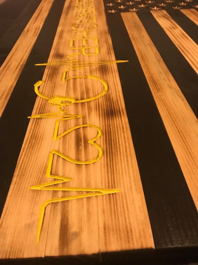 K&ouml;nnte beinhalten: Eine amerikanische Flagge aus Holz mit schwarzen und gelben Streifen. Die Flagge hat eine gelbe Inschrift mit der Aufschrift "523".