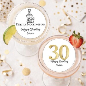 May include: Two cocktails, one a margarita with a lime wedge, the other a pink drink with a strawberry garnish. Both have white circles with text. One says "Tequila Mockingbird Happy Birthday Susan", the other has a gold "30" and "Happy Birthday Susan".