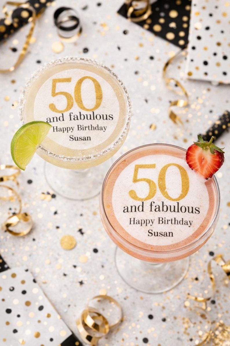 May include: Two margarita glasses with the text "50 and fabulous Happy Birthday Susan" in gold. One glass has a lime wedge, the other a strawberry. The background is white with gold confetti and ribbons.
