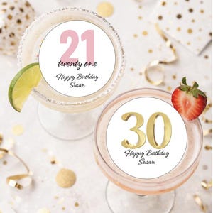 May include: Two cocktails with birthday decorations. One glass has a lime wedge and a circle with the number "21" and the text "twenty one Happy Birthday Susan". The other glass has a strawberry and a circle with the number "30" and the text "Happy Birthday Susan".