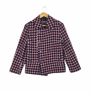 May include: A double-breasted blazer with a geometric pattern in navy blue, red, and white. The jacket has long sleeves and is hanging on a wooden hanger. The blazer has a classic collar and button closures.