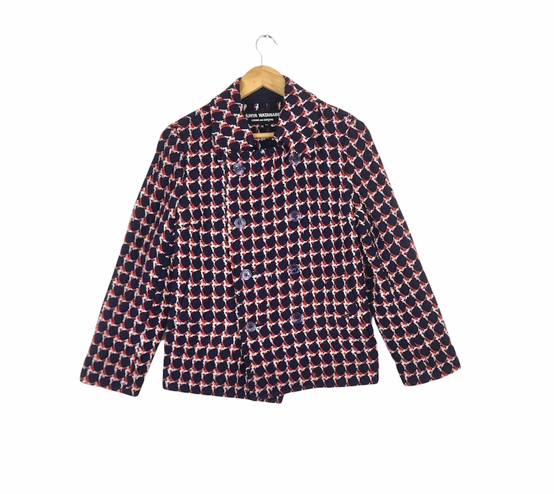 May include: A double-breasted blazer with a geometric pattern in navy blue, red, and white. The jacket has long sleeves and is hanging on a wooden hanger. The blazer has a classic collar and button closures.