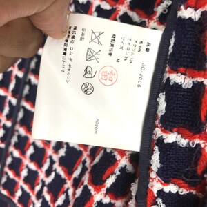 May include: Close-up of a woven fabric with a diamond pattern in navy blue, red, and white. A white tag with Japanese text and care symbols is attached to the fabric. The tag includes the product code JC-J006.