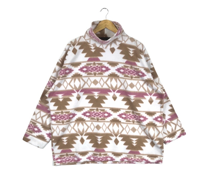 Puede incluir: Sudadera de vell&oacute;n blanca con un patr&oacute;n geom&eacute;trico marr&oacute;n y rosa.