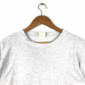 May include: A heather grey t-shirt with a crew neck. The shirt is hanging on a wooden hanger.
