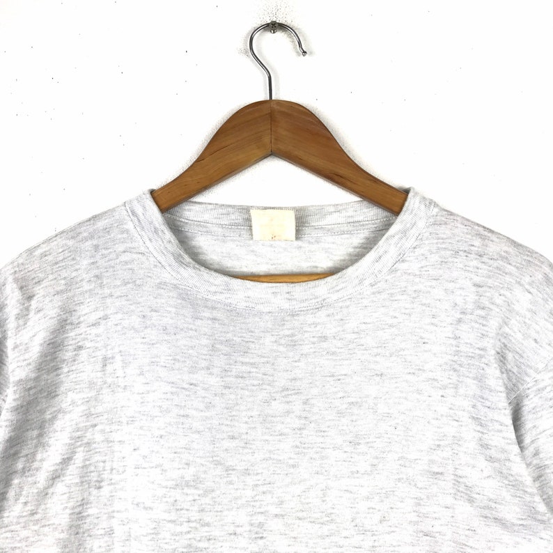 May include: A heather grey t-shirt with a crew neck. The shirt is hanging on a wooden hanger.