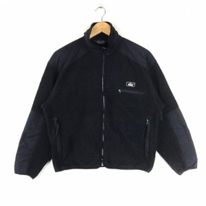 May include: Black fleece jacket with a zipper closure and a small logo patch on the left chest. The jacket has two zippered pockets on the front and a stand-up collar.