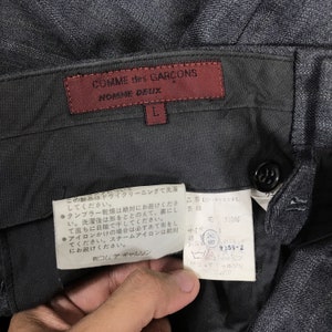 May include: A pair of black trousers with a red label that reads "COMME des GAR&Ccedil;ONS NOMORE DEUX" and a white label with Japanese text and care instructions.