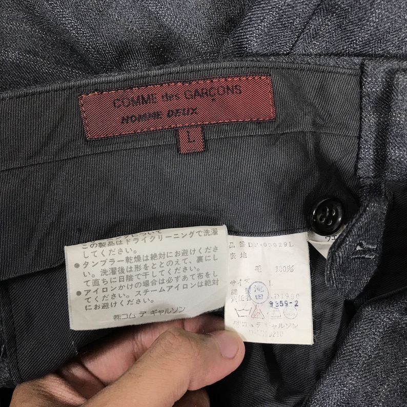 May include: A pair of black trousers with a red label that reads "COMME des GAR&Ccedil;ONS NOMORE DEUX" and a white label with Japanese text and care instructions.