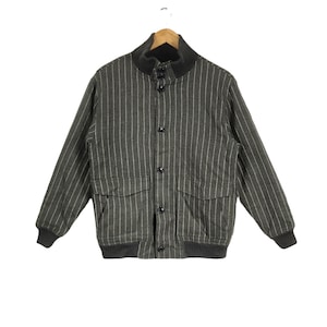 Puede incluir: Una chaqueta gris a rayas con cierre de botones y dos bolsillos grandes. La chaqueta tiene un cuello y puños de punto de canalé.