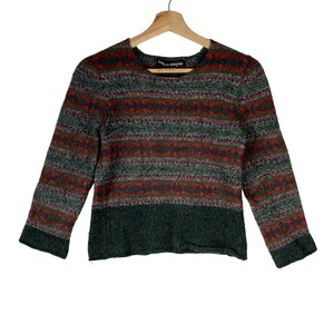 May include: A striped sweater with a green, red, and white color scheme. The sweater has a crew neck and long sleeves. The sweater is made of a soft, fuzzy material.
