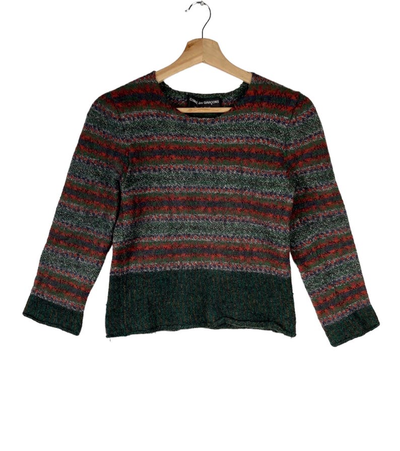 May include: A striped sweater with a green, red, and white color scheme. The sweater has a crew neck and long sleeves. The sweater is made of a soft, fuzzy material.