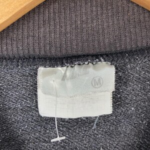 May include: Close-up of a black sweatshirt with a white tag that says "M" on it.