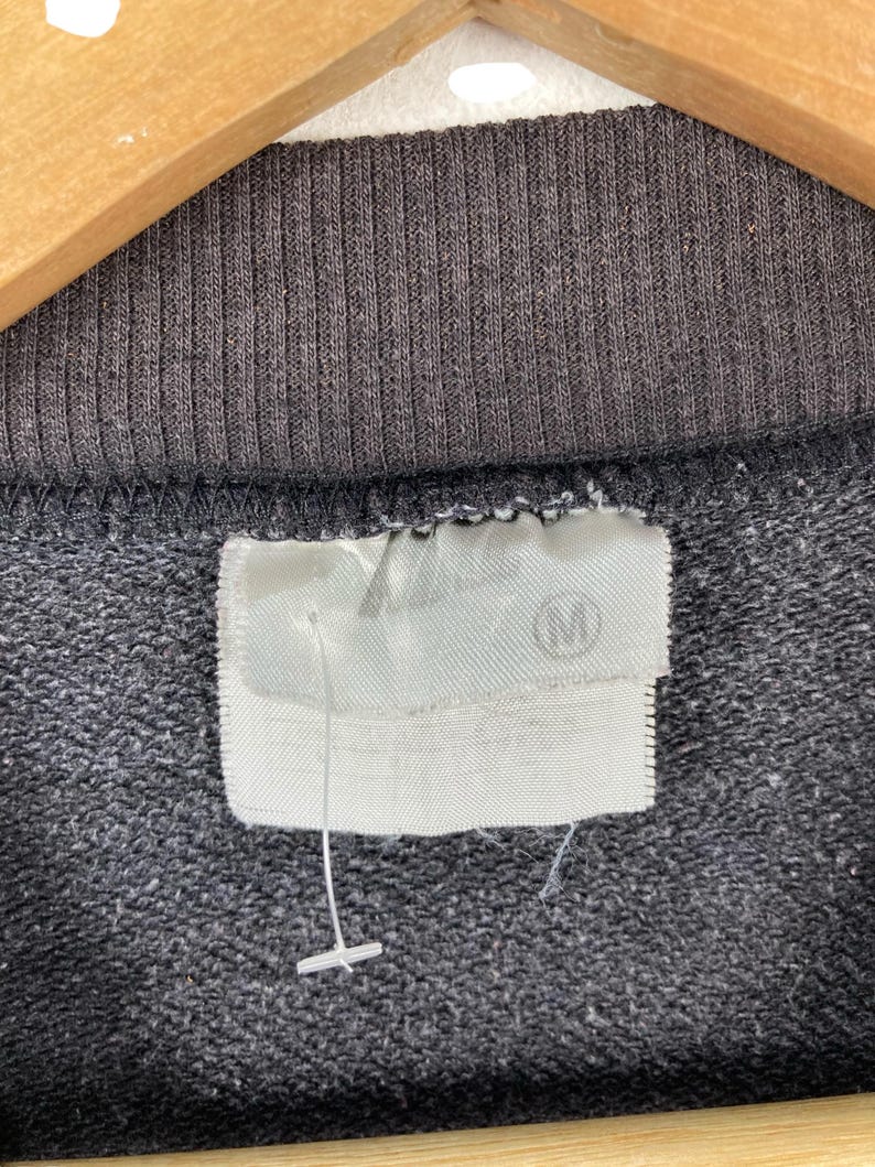May include: Close-up of a black sweatshirt with a white tag that says "M" on it.