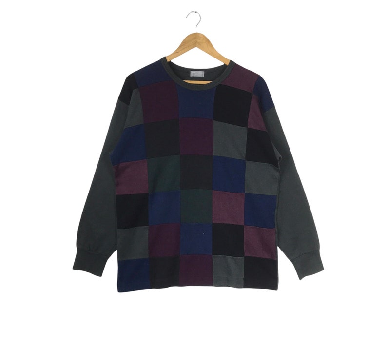 Puede incluir: Un su&eacute;ter de manga larga con un dise&ntilde;o de patchwork. El su&eacute;ter est&aacute; hecho de una tela suave y c&oacute;moda y presenta una variedad de colores, incluyendo negro, gris, azul y morado.