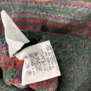 May include: A close-up of a black and white label with the text "COMME des GAR&Ccedil;ONS Co., Ltd. MADE IN JAPAN FABRIQUE AU JAPON PN-040140 ALBASA 100% WOOL LAINE 30% AL DO NOT BLEACH COOL IRON DRY CLEAN ONLY JAVEL INTERDIT FER DOUX NETTOYAGE A SEC"