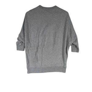以下が含まれることがあります： クルーネックと七分袖のグレーのスウェットシャツ。衣服の背面が見え、中央に縫い目があります。生地は柔らかく快適な素材のようです。