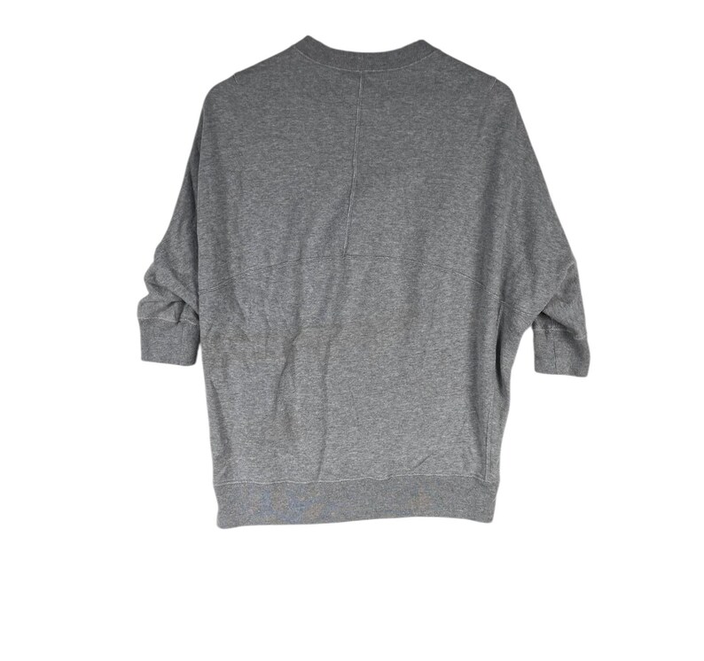 以下が含まれることがあります： クルーネックと七分袖のグレーのスウェットシャツ。衣服の背面が見え、中央に縫い目があります。生地は柔らかく快適な素材のようです。