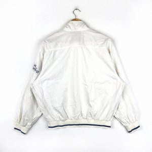 May include: White windbreaker jacket with blue trim and the text "Lacoste Sport" on the sleeve.