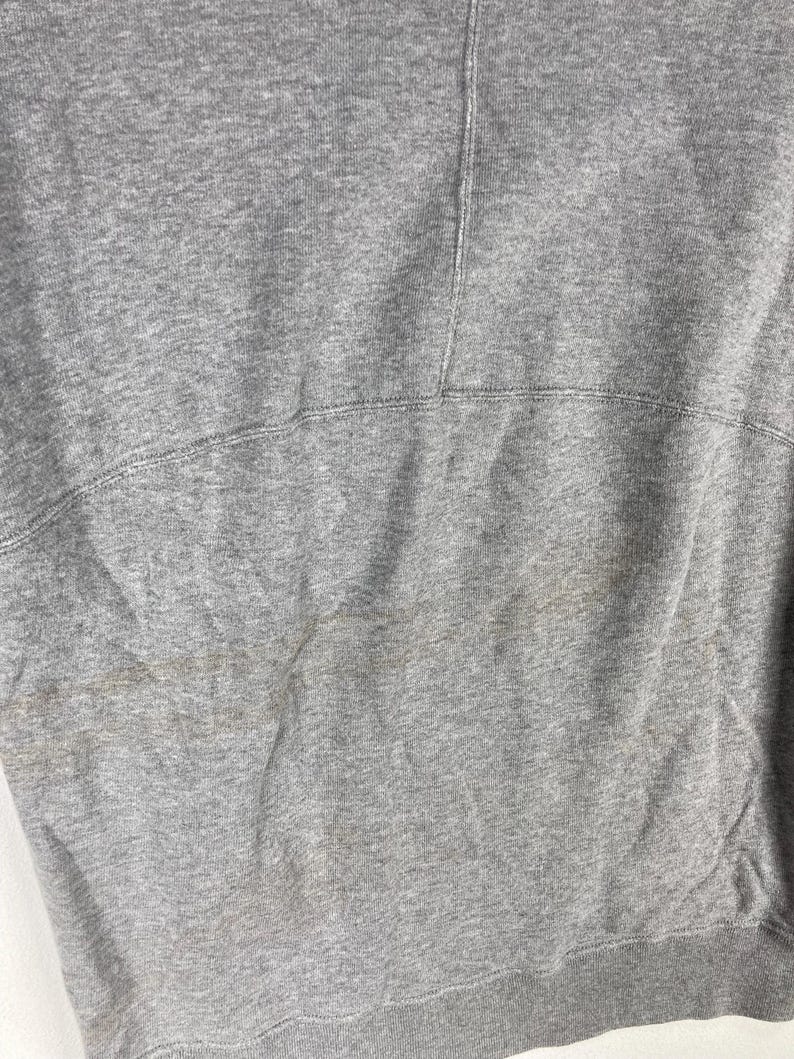 以下が含まれることがあります： 杢グレーのスウェットシャツのクローズアップ。生地は、縫い目に沿ってステッチが見える、テクスチャ加工された外観をしています。裾とネックラインが見えます。スウェットシャツは使い古されているようです。