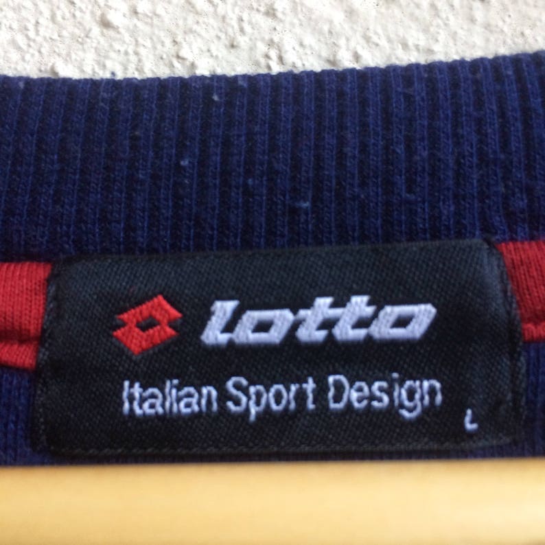 May include: A black and white label with the text "lotto" in white and "Italian Sport Design" in gray. The label has a red diamond logo with a white outline.